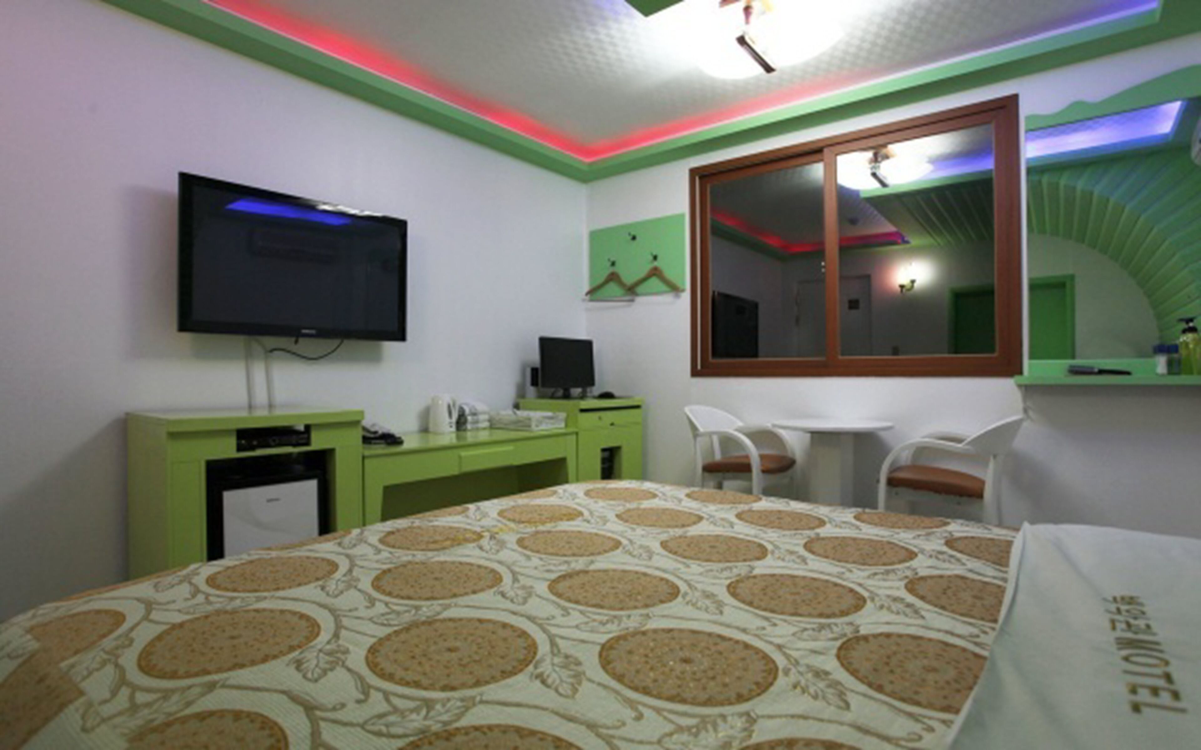 A hotel room with a bed, a desk, a chair, a television, and a window with a view of the sky.