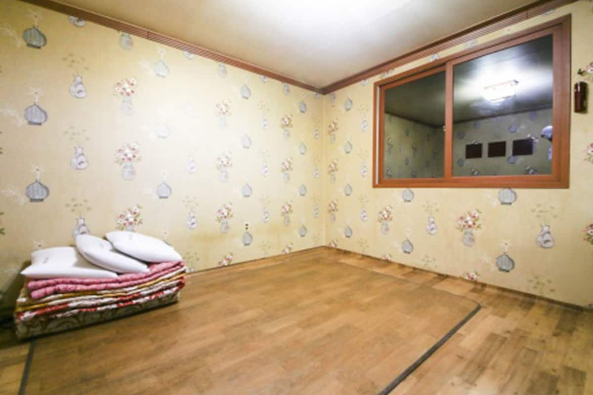 A room with patterned wallpaper, a wooden floor, and a window with blinds.