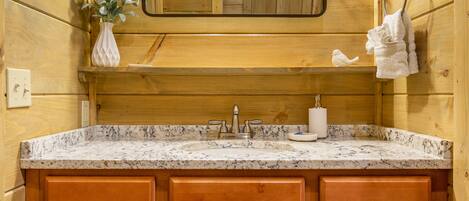 Un baño estilo cabaña de madera con lavamanos de granito, armarios de madera, un espejo y un perchero para toallas.