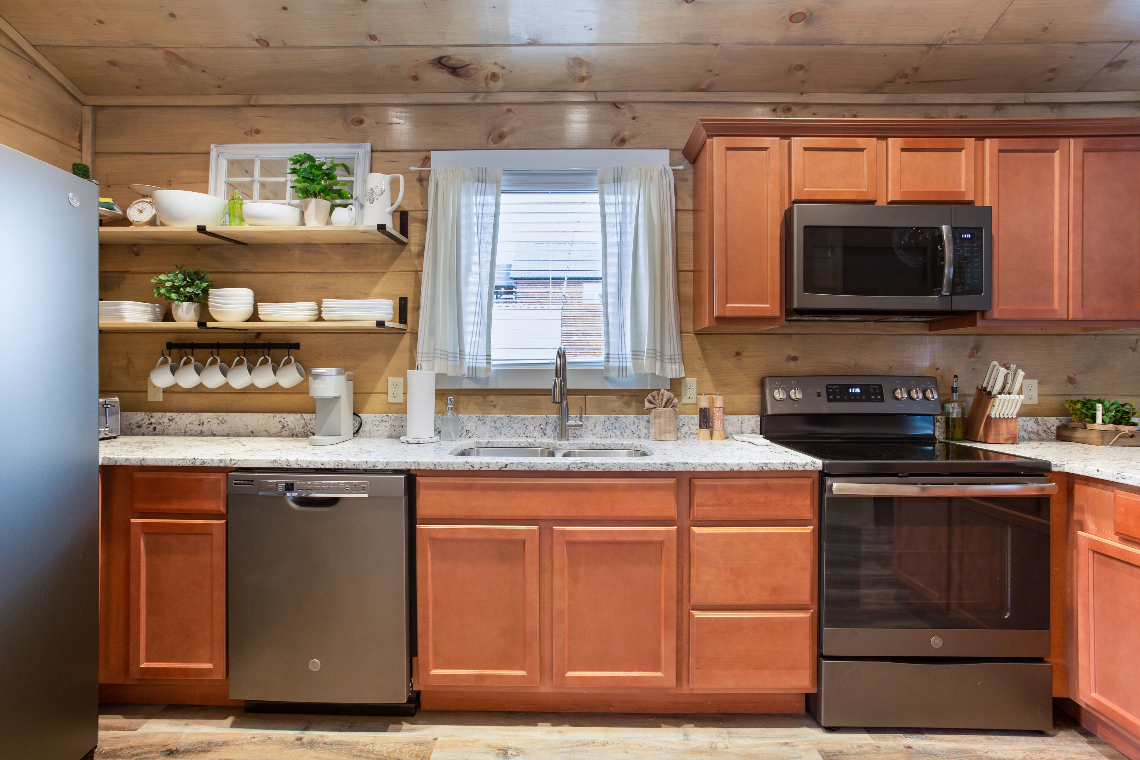 A modern kitchen with wooden cabinets, stainless steel appliances, and a window with curtains.