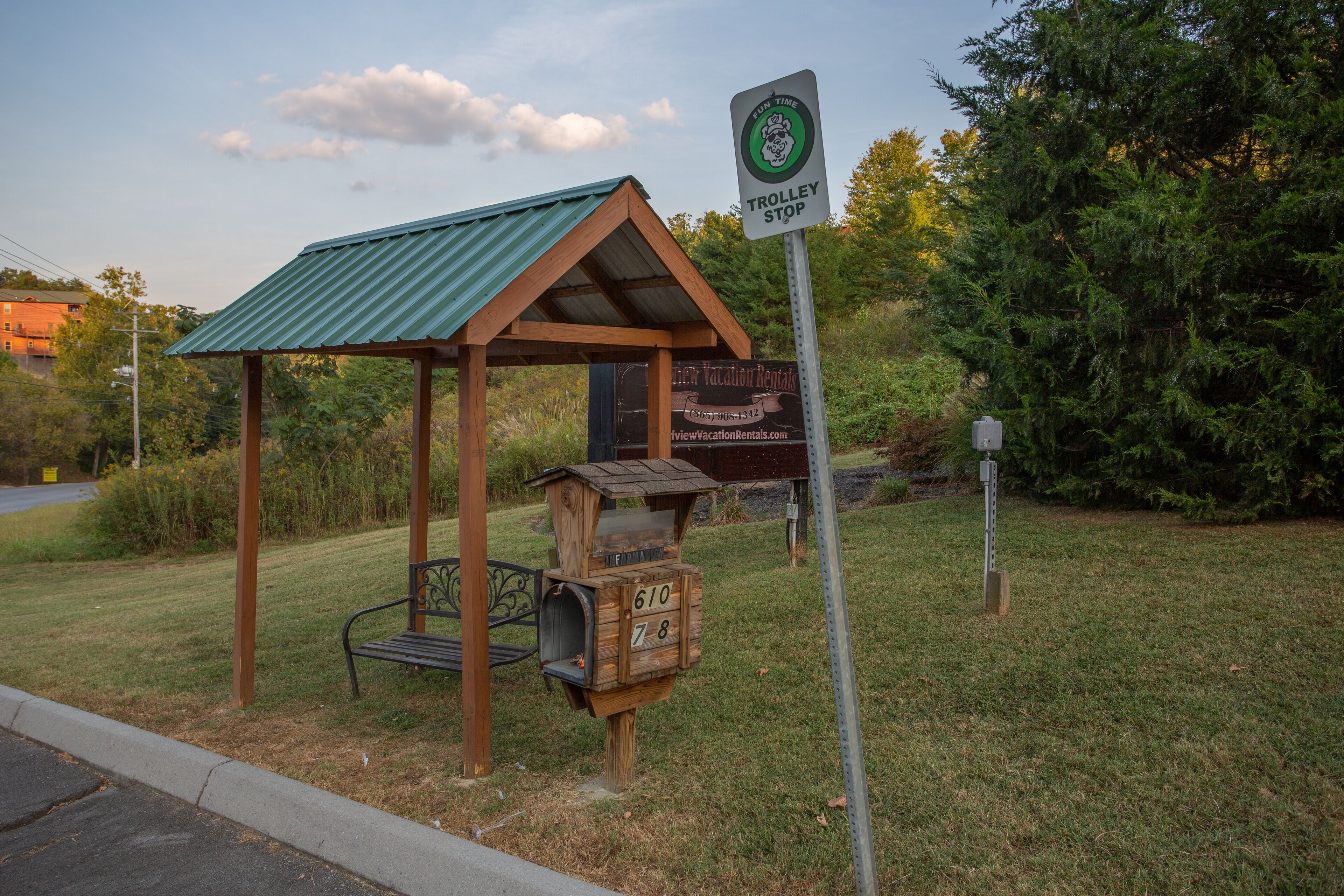 A wooden gazebo with a green roof, a mailbox, and a sign for a trolley stop.