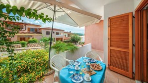 Un patio con una mesa lista para dos personas, rodeado de un jardín con flores de naranja y vistas a casas vecinas.