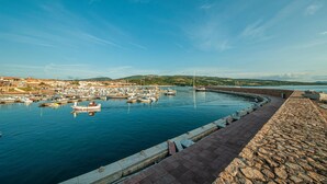 Un puerto costero con barcos amarrados, un muelle de piedra y un paisaje montañoso al fondo.