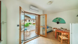 Un espacio habitable compacto con una puerta corrediza de vidrio que da a un balcón, una zona de comedor con mesa y sillas, y una cocina con refrigerador.