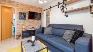 A living room with a blue sofa, patterned cushions, a small table with a candle, and a brick wall.