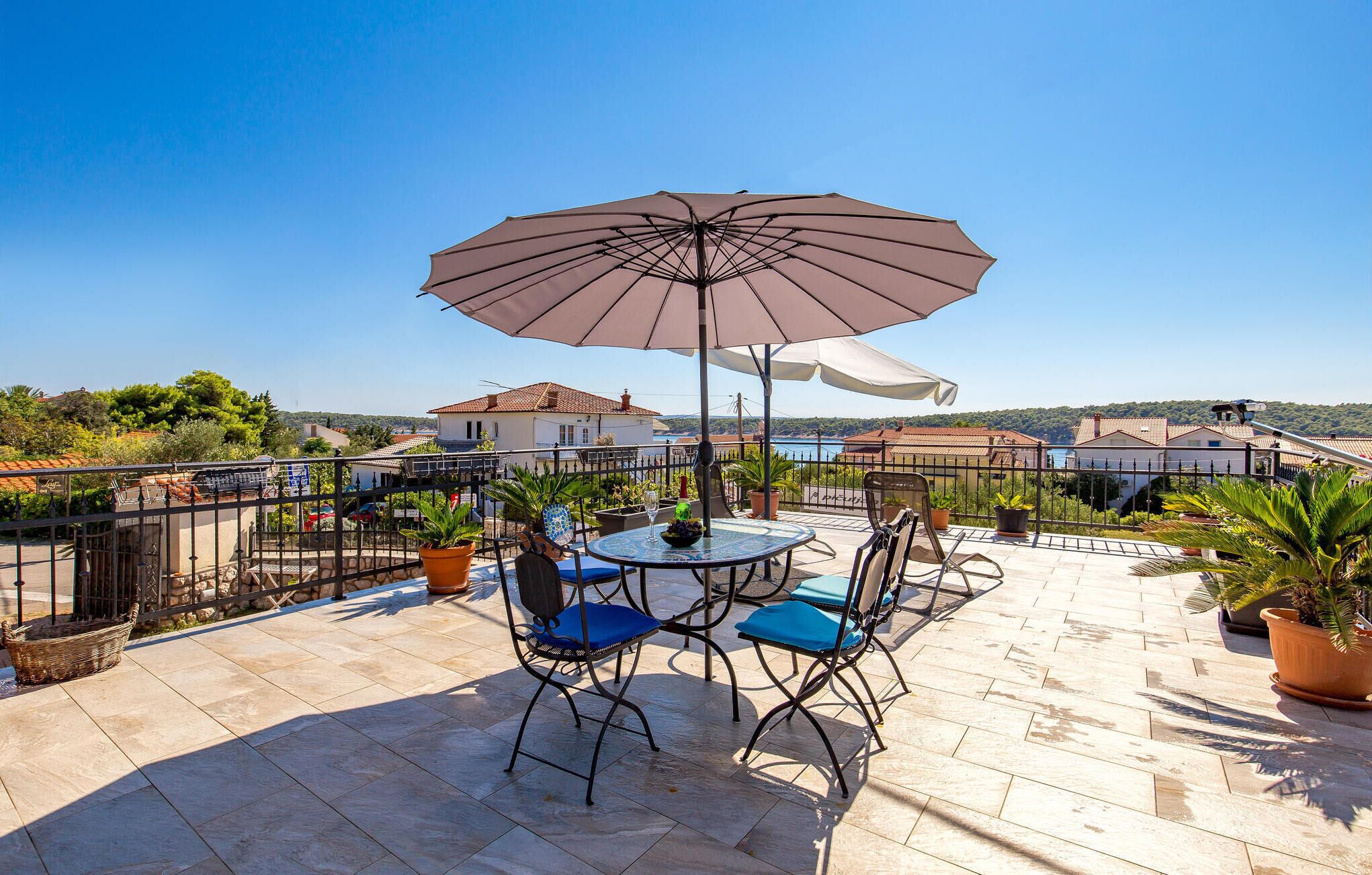 A patio with a round table and chairs, a large umbrella, and potted plants.