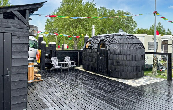 A wooden deck with a sauna, two Adirondack chairs, and a small table.
