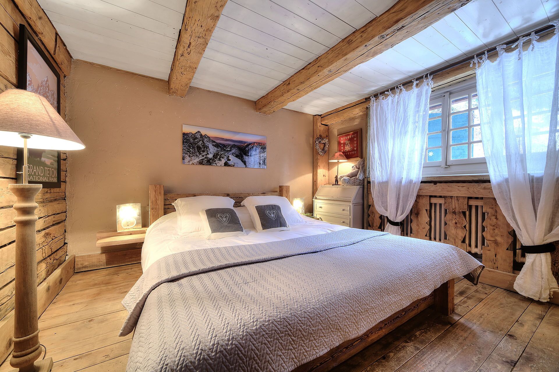 A cozy bedroom with a wooden bed, a nightstand, a lamp, and a window with curtains.