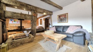 A rustic living room with exposed wooden beams, a black leather sofa, a wooden coffee table, and a painting on the wall. - Authentic, warm, luxurious chalet, swimming pool, jacuzzi, sauna and fireplace (Les Contamines-Montjoie)