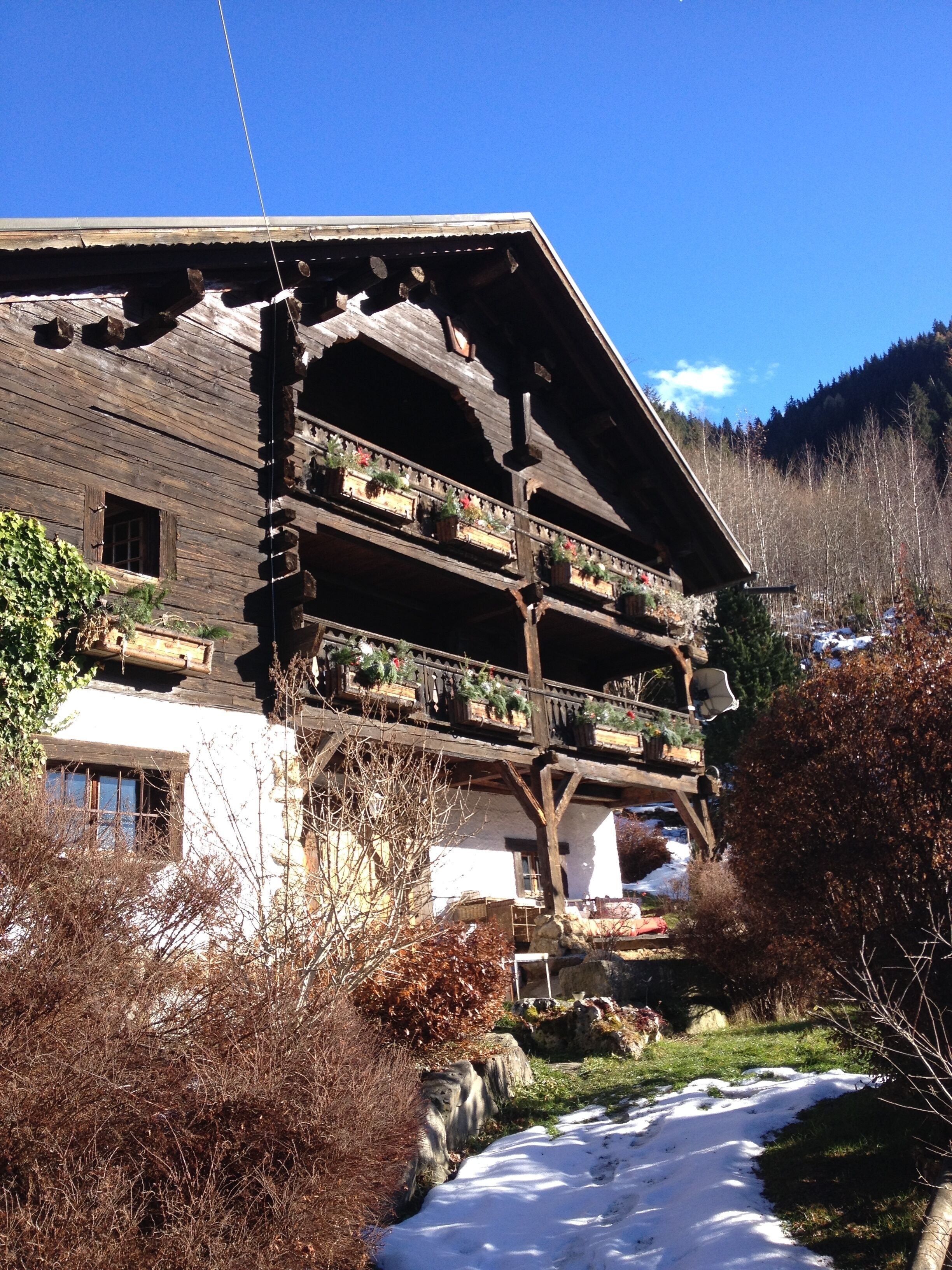 Una caba ña de madera tradicional con varios balcones, un cimiento de piedra y un camino cubierto de nieve que lleva a ella.