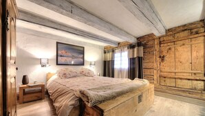 A rustic bedroom with a wooden bed, a nightstand, a lamp, and a large window with curtains. - Authentic, warm, luxurious chalet, swimming pool, jacuzzi, sauna and fireplace (Les Contamines-Montjoie)
