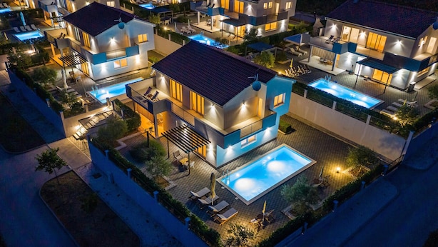 Un complexe résidentiel moderne comprenant plusieurs maisons à deux étages, chacune dotée d’un balcon et d’une piscine.