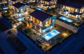 Un complexe résidentiel moderne comprenant plusieurs maisons à deux étages, chacune dotée d’un balcon et d’une piscine.