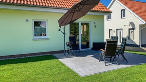 Une maison dotée d’un patio comprenant deux chaises et une table, une porte-fenêtre coulissante et une antenne parabolique.