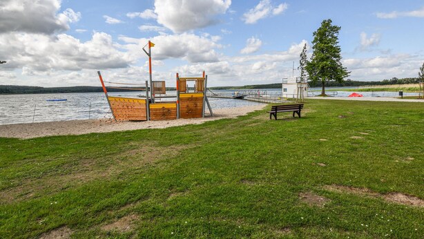 Une plage avec un poste de surveillance en bois, un banc et un arbre.