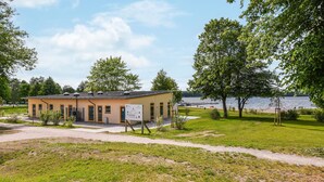 Un petit bâtiment d’un seul étage, doté d’un toit plat, entouré d’une pelouse et d’arbres.