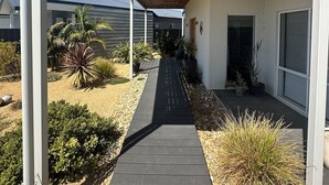 A covered walkway leading to a modern house with a wooden ceiling, surrounded by landscaped gardens and potted plants. - Room to relax in a perfect location with an easy walk to the beach and shops. (Normanville)