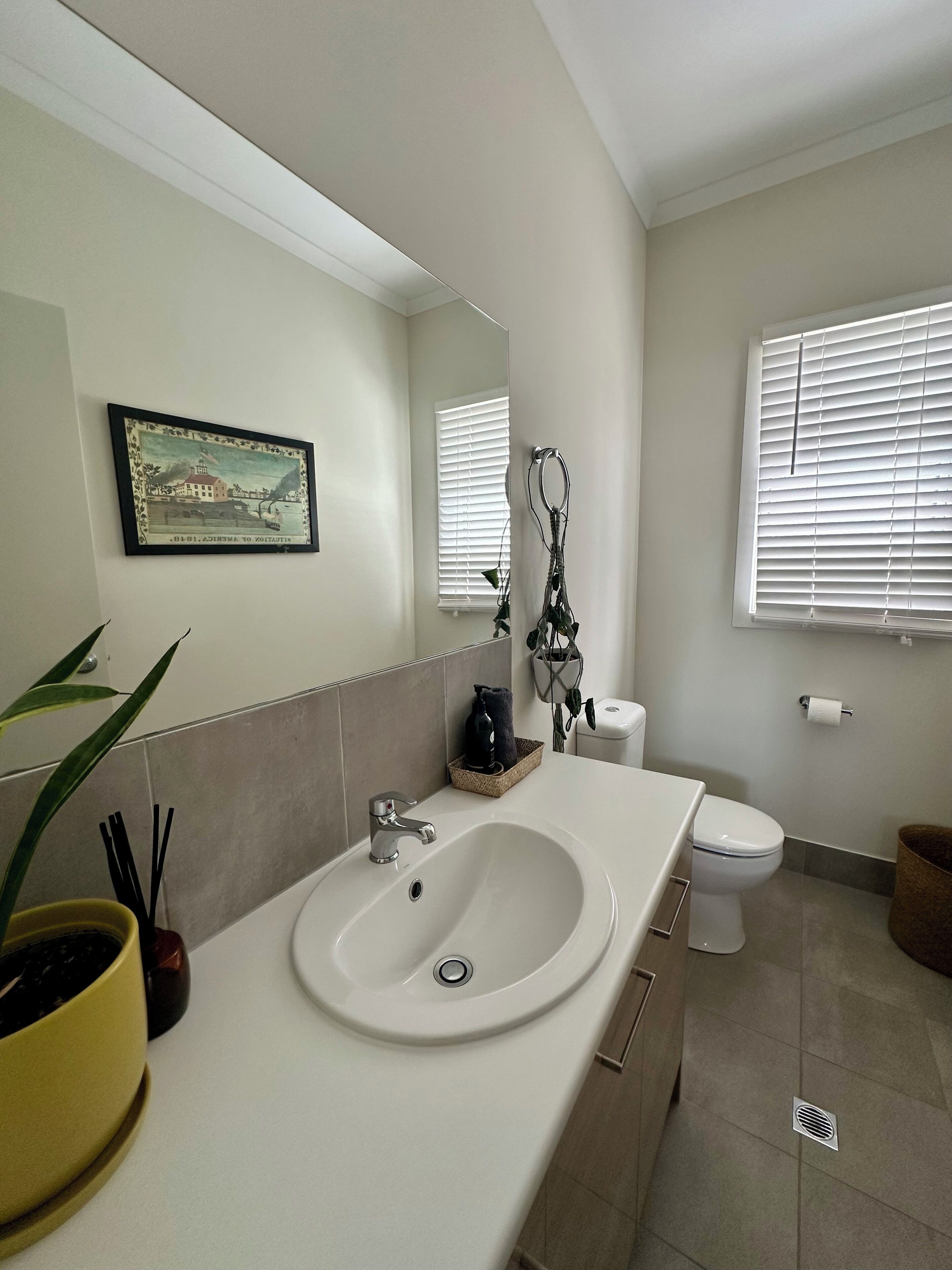 A modern bathroom with a white sink, a toilet, and a window with blinds.