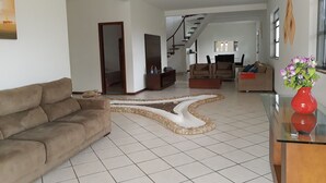 A spacious living room with a modern design, featuring a brown sofa, a glass coffee table, and a unique white and beige rug. - Your best season in Gabriela's land (Ilhéus)