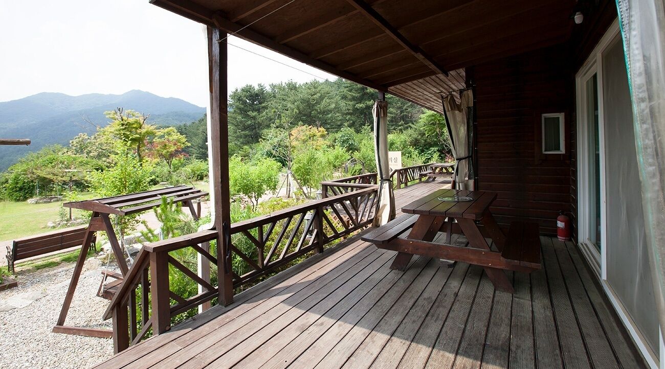 Una terraza de madera con mesas de picnic y bancos, con vistas a un paisaje montañoso.