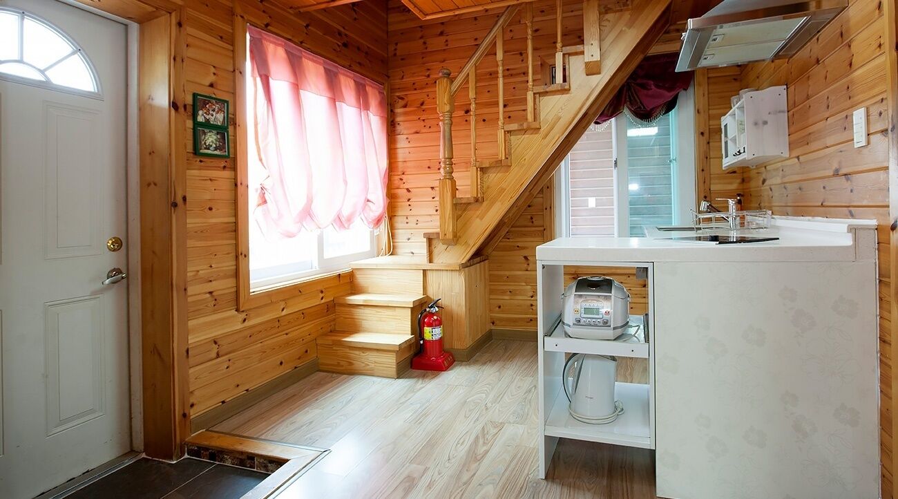 A wooden cabin interior with a kitchen area, a staircase, and a fire extinguisher.