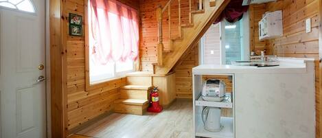 A wooden cabin interior with a kitchen area, a staircase, and a fire extinguisher.
