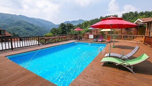 A swimming pool with a wooden deck, lounge chairs, and red umbrellas. - Laviche Pension (Gapyeong)