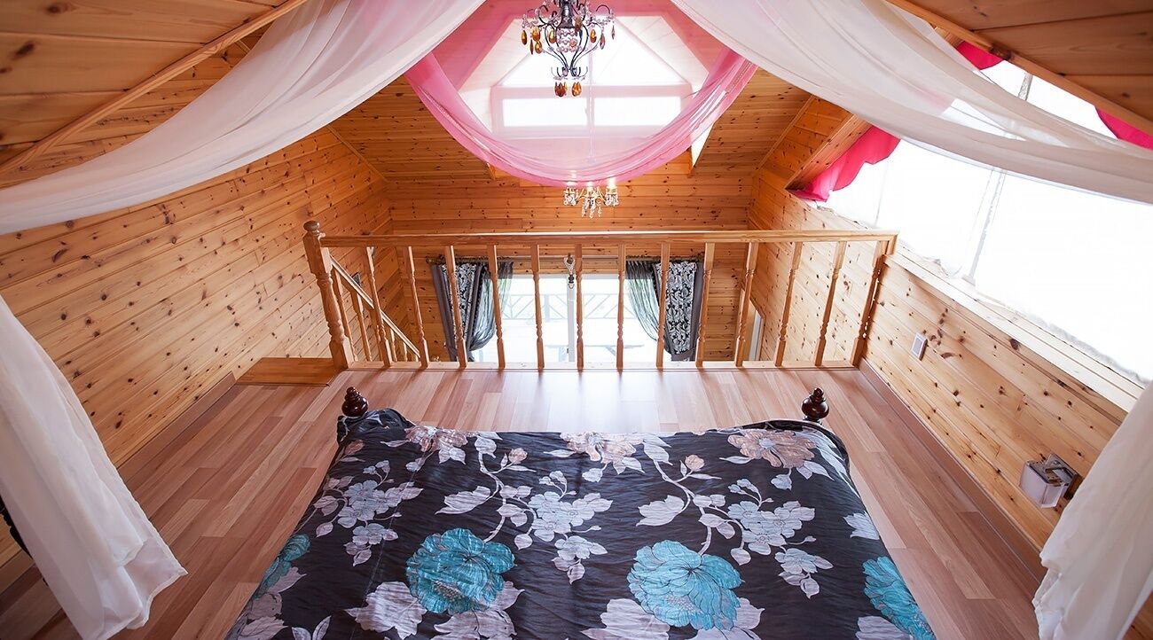Un dormitorio acogedor en el ático con suelo de madera, una cama con colcha estampada, una araña y un balcón con cortinas.