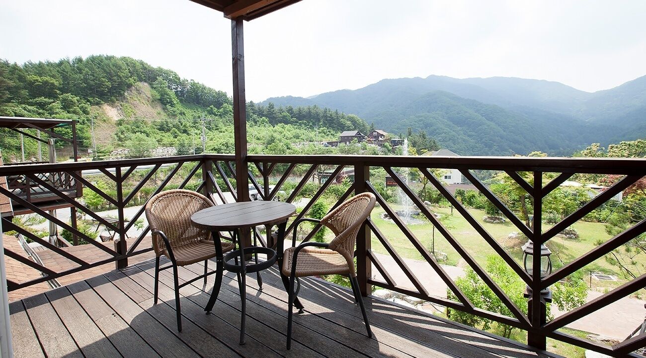 Una terraza de madera con sillas de mimbre y una mesa, con vistas a un paisaje montañoso.