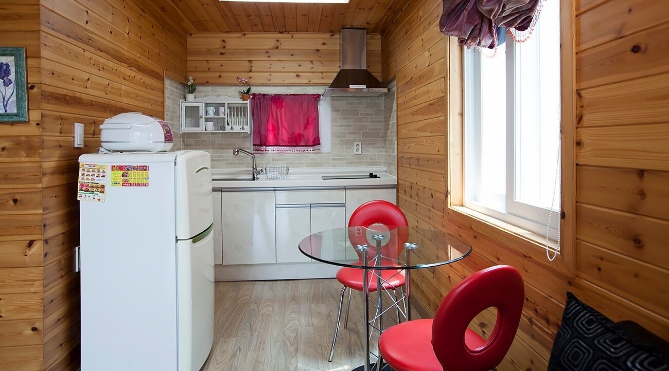 Eine kleine Küche mit Holzwänden, einem Kühlschrank, einer Spüle und einem Essbereich mit einem Glastisch und roten Stühlen.