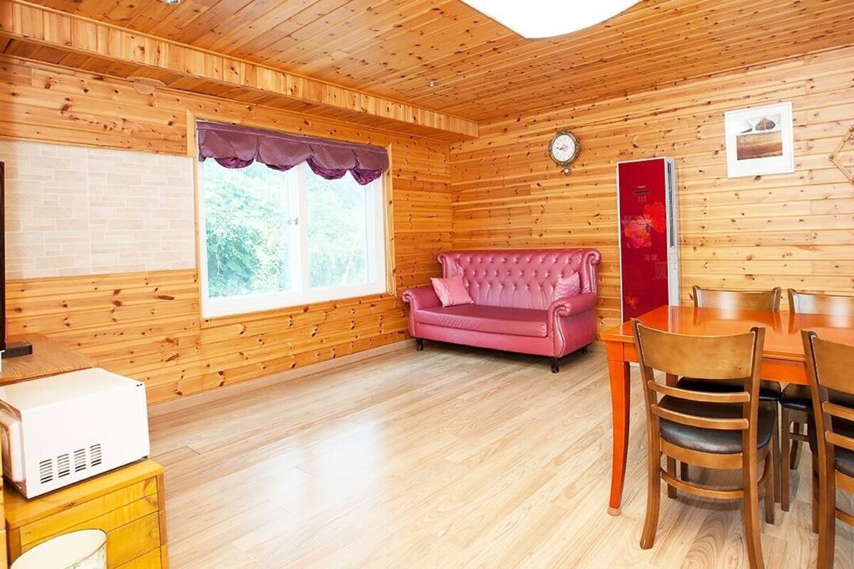 A cozy cabin interior with a wooden interior, a pink sofa, a dining table with chairs, and a refrigerator.