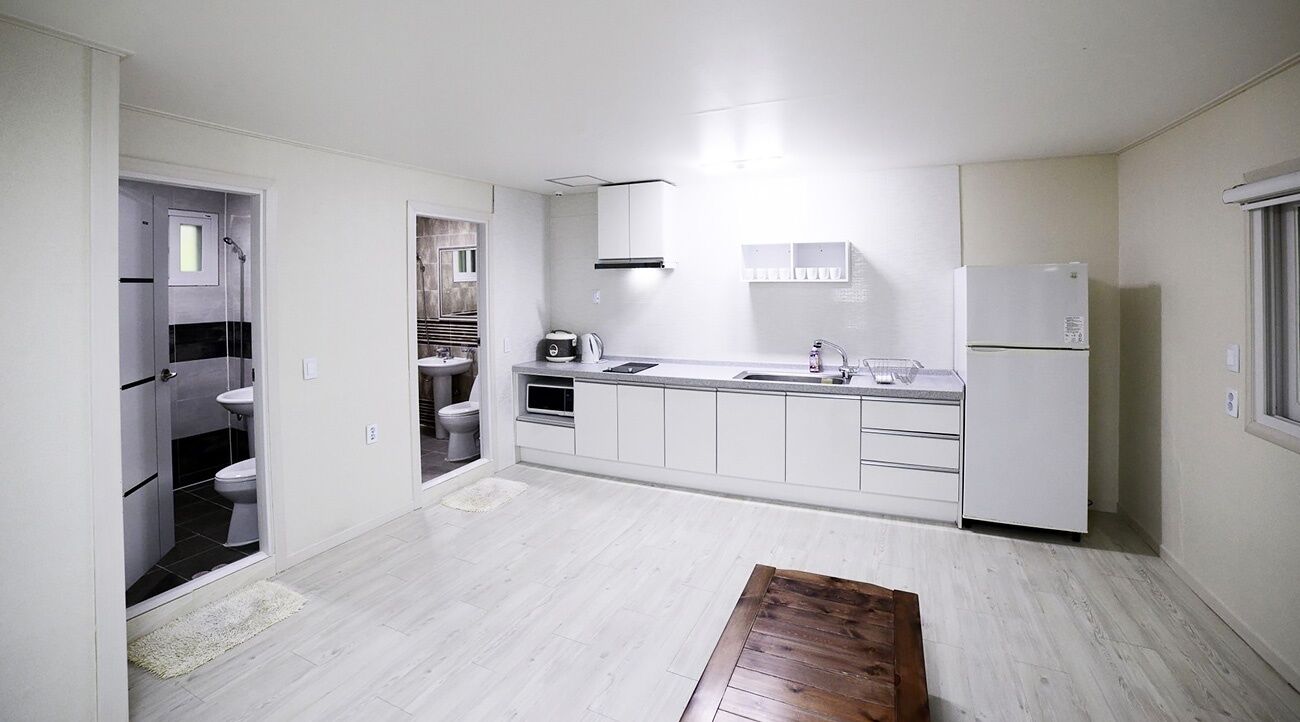A modern kitchen with white cabinets, a sink, a refrigerator, and a wooden table.