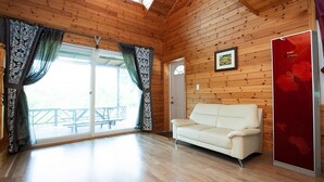 A wooden cabin with a white sofa, a red refrigerator, and a door with a picture on the wall. - Laviche Pension (Gapyeong)