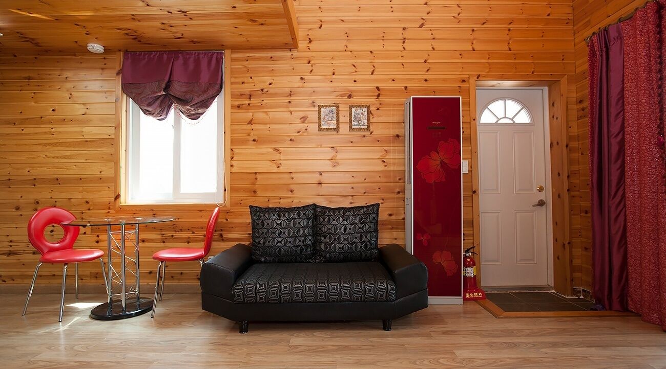 L’intérieur d’un chalet en bois, avec un canapé, des chaises rouges, une petite table et une porte surmontée d’un rideau rouge.