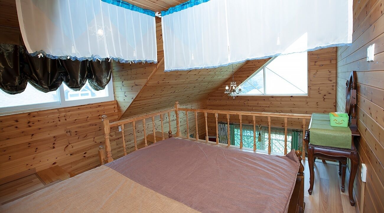A wooden cabin bedroom with a bed, a bench, and a window with curtains.