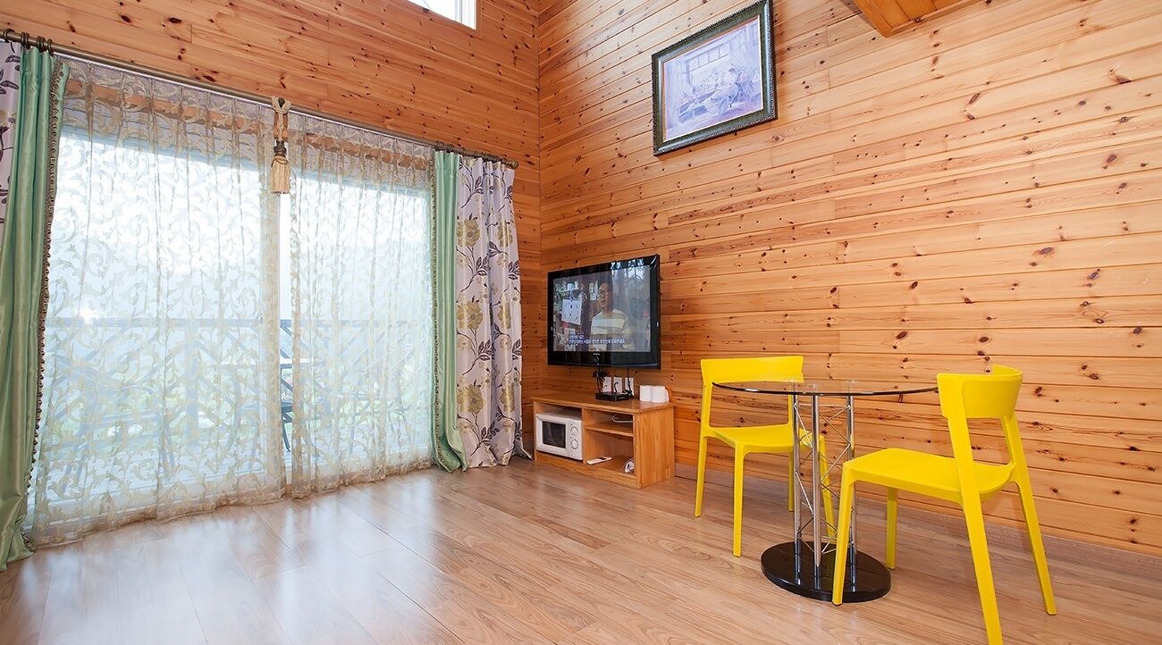 A wooden-paneled room with a TV, yellow chairs, and a small table.