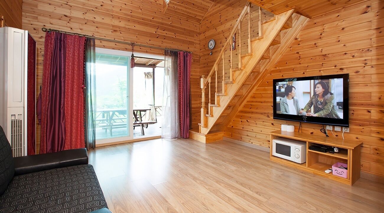 Un interior de madera con televisor, sofá y escalera.