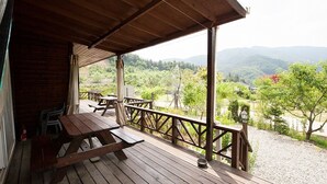 A wooden deck with picnic tables and a view of a mountainous landscape. - Laviche Pension (Gapyeong)