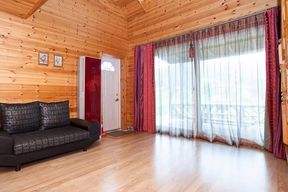 A wooden cabin interior with a black sofa, red chair, and a door leading outside.