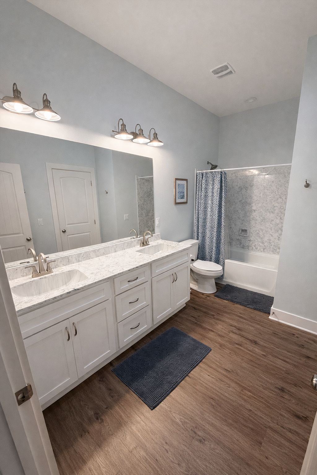 A bathroom with a double sink vanity, a toilet, a bathtub, and a shower curtain.