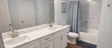 Un baño con tocador de doble lavabo, inodoro, bañera y cortina de ducha.