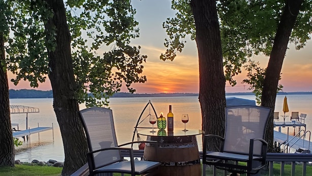 Um deck com duas cadeiras e um barril, com vista para um pôr do sol sobre a água.