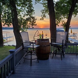 Une terrasse avec deux chaises et un tonneau, d’où l’on peut admirer un coucher de soleil sur une étendue d’eau.