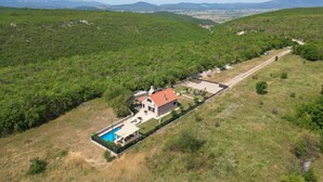 Une maison avec une piscine, entourée d’une cour clôturée et donnant sur une route.