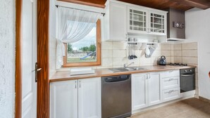 Une cuisine moderne avec des meubles blancs, un lave-vaisselle, une cuisinière et une fenêtre donnant sur un terrain de jeux.