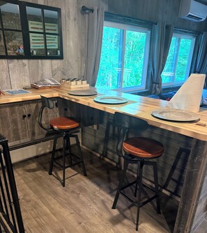 A kitchen with wooden countertops, two stools, a window with curtains, and a wall-mounted air conditioning unit.
