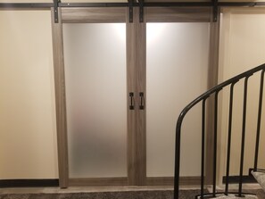 Een houten garderobe met twee deuren en een handgreep, een vloer met tapijt en een metalen trapleuning.