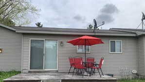 Une maison mobile dotée d’un patio comprenant une table et des chaises, un parasol rouge et une porte-fenêtre coulissante.