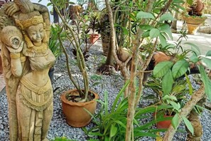 A statue of a figure with a child, surrounded by potted plants and trees. - Ban Elephant Blanc Bungalow (Karon)