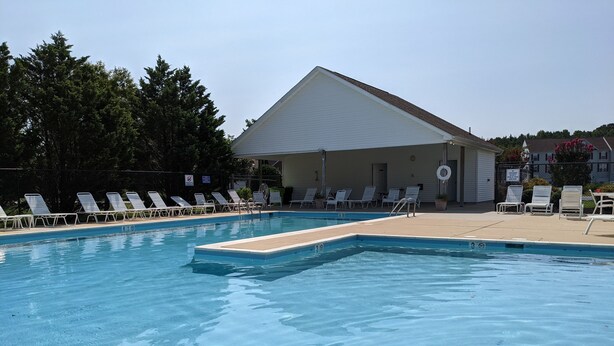 Piscina com cadeiras de descanso brancas e um edifício ao fundo.